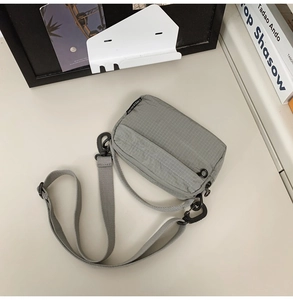 Detail of gray-green mini crossbody bag featuring ripstop nylon fabric and zipper pockets