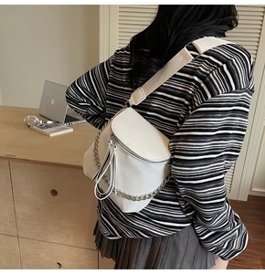 White saddle chest bag with silver chain detail and wide strap worn by a model