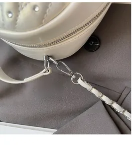 Detail of white quilted handbag with silver studs and metal chain strap on a gray blazer
