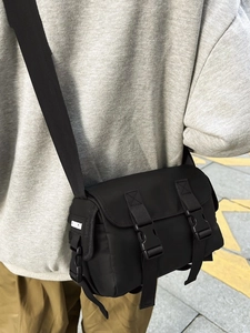 Street style black nylon messenger bag with flap closure and adjustable shoulder strap