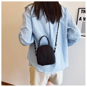 Detail of black mini crossbody bag with woven rope handle and metal logo on a model