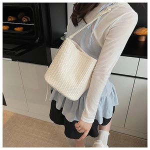 Détail du sac seau blanc tressé montrant la texture croisée et la bandoulière fine