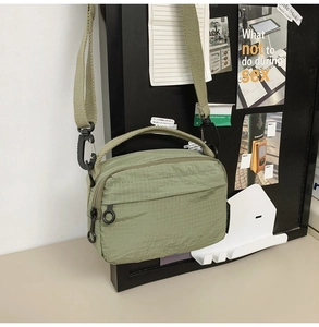 Detail of light green ripstop nylon crossbody bag with dual zippers and woven strap