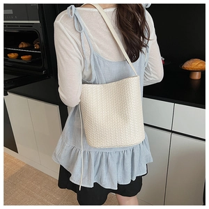 Détail du sac seau tressé crème avec longue bandoulière dans un décor moderne chic
