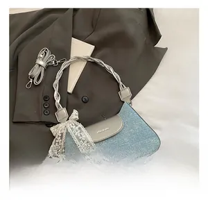 Détail du sac baguette en denim bleu avec garniture en cuir argenté et nœud en dentelle