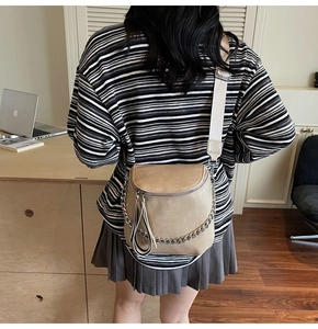 Detail of beige saddle bag featuring pebble leather, wide strap, and silver chain decor