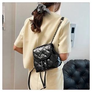 Rear view of a model wearing a small black quilted backpack with silver lock and chain straps