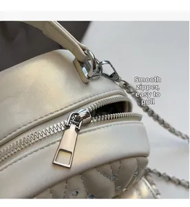Detail of smooth gold-tone metal zipper on ivory quilted leather backpack with rhinestones