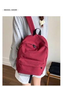 Side view of a burgundy canvas backpack with front zipper pocket on a model for daily use