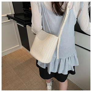 Détail d'un sac seau tressé crème avec texture à chevrons porté à l'épaule par un mannequin