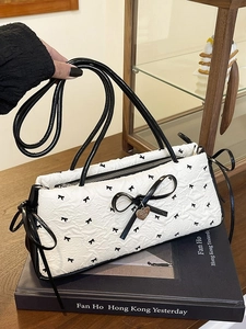Chic black and white bow shoulder bag with heart pendant on a vintage book setting