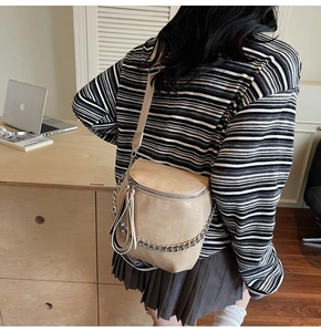 Close-up of beige leather saddle bag featuring chunky silver chain and tassel detail