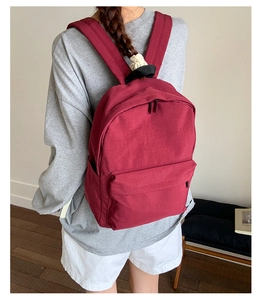 Detail view of burgundy minimalist backpack showing front zipper pocket and durable canvas texture