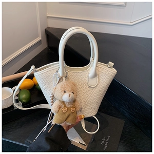 Détail du sac seau blanc motif crocodile avec breloque d'ours sur un escalier noir