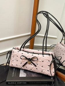 Pink pleated crossbody bag with black bow prints and golden heart pendant on a magazine