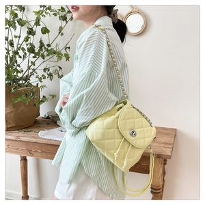 Detail of light yellow quilted backpack featuring chain strap and metallic turn-lock closure