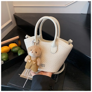 Détail d'un sac seau blanc texture crocodile avec pendentif ours sur escalier moderne