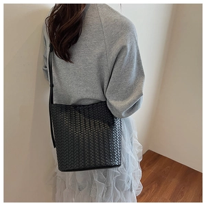 Detail of a black woven leather bucket bag worn crossbody with an intricate weave texture