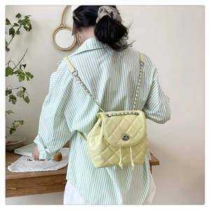 Detail of light green quilted leather backpack with gold chain strap worn by a model