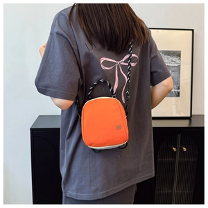 Detailed shot of an orange and white crossbody bag with woven rope handle and metal logo