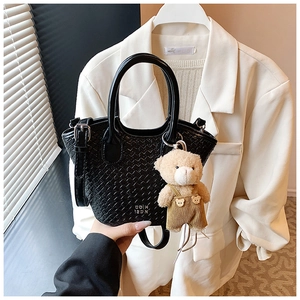 Détail du sac seau noir tressé avec logo blanc et pendentif ours en peluche mignon