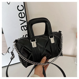 Detail view of glossy black quilted pillow bag with silver chain strap and top handle