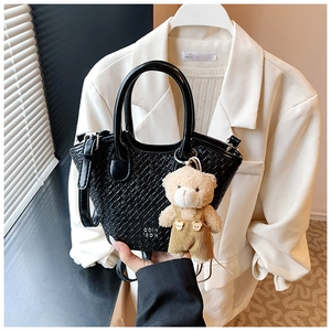 Détail d'un mini sac seau tressé noir avec un petit ours en peluche et logo gravé