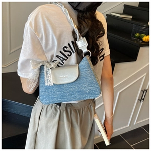 Détail du sac sous le bras en denim bleu avec rabat en cuir argenté et bandoulière tressée