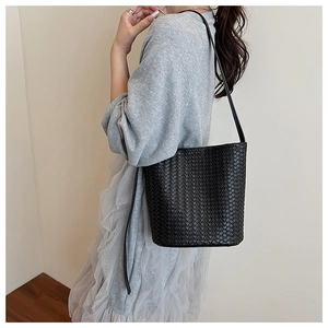 Detail of a black woven bucket bag showing intricate leather texture and shoulder strap