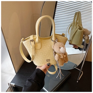 Détail du sac seau crème avec texture tressée et petit pendentif ours brun