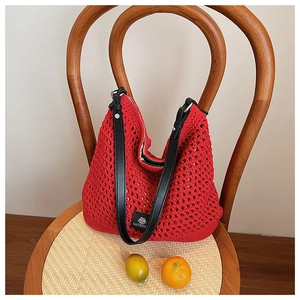 Détail du sac à main tissé rouge avec des anses en cuir noir sur une chaise en bois