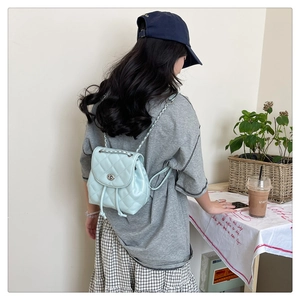 Detail of light blue quilted mini backpack with metal chain straps on a female model
