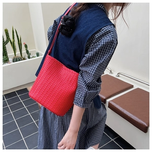 Détail du sac seau rouge tressé avec texture de cuir artisanale porté par une femme