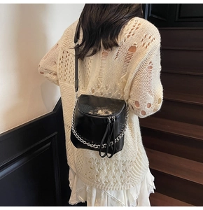 Glossy black saddle bag with silver chain strap shown worn on a model in a stairwell