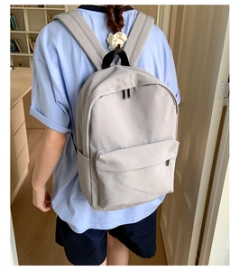 Detail view of a light grey canvas backpack with spacious main compartment and front pocket