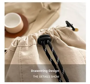 Detail view of beige nylon bucket bag featuring drawstring closure and black cord lock