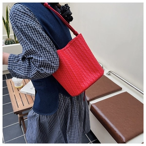Détail du sac seau tressé en cuir rouge avec fine bandoulière en scène urbaine