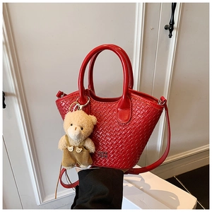 Détail du sac seau rouge tressé avec finition lisse et pendentif ours en peluche mignon