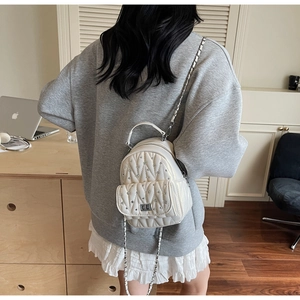 Detail of cream quilted mini backpack with silver studs, metal handle and chain straps
