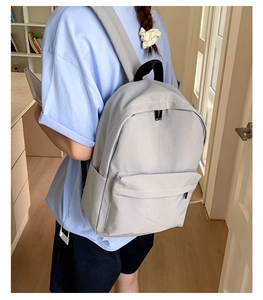 Rear view of a light gray minimalist backpack worn over a blue T-shirt in a home setting