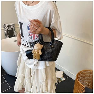 Détail du mini sac seau tressé noir avec un charm ours en peluche et une poignée ronde
