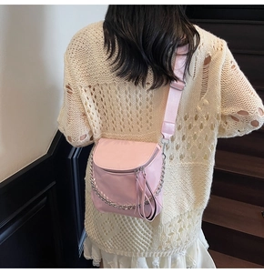 Close-up of pink glossy saddle bag with silver chain and wide textile shoulder strap