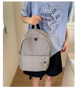 Detail of light gray canvas backpack featuring white stitched front pocket and durable handles