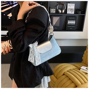 Detail of light blue denim shoulder bag featuring silver metallic flap and white lace bow