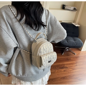 Detail of cream quilted mini backpack with rhinestone accents and silver chain straps