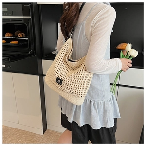 Détail du sac de plage au crochet avec un écusson logo en cuir noir sur tissu tissé beige