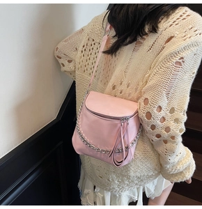 Detail of light pink saddle bag with silver chain and long zipper pulls on a model