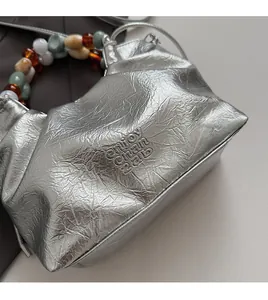 Detail view of the silver pleated bucket bag featuring a colorful beaded handle and logo