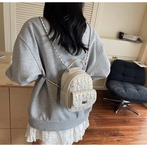 Detailed back view of a beige quilted mini backpack with rhinestone studs and chain strap