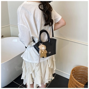 Détail du sac bandoulière noir tressé avec breloque ours porté par un mannequin en décor